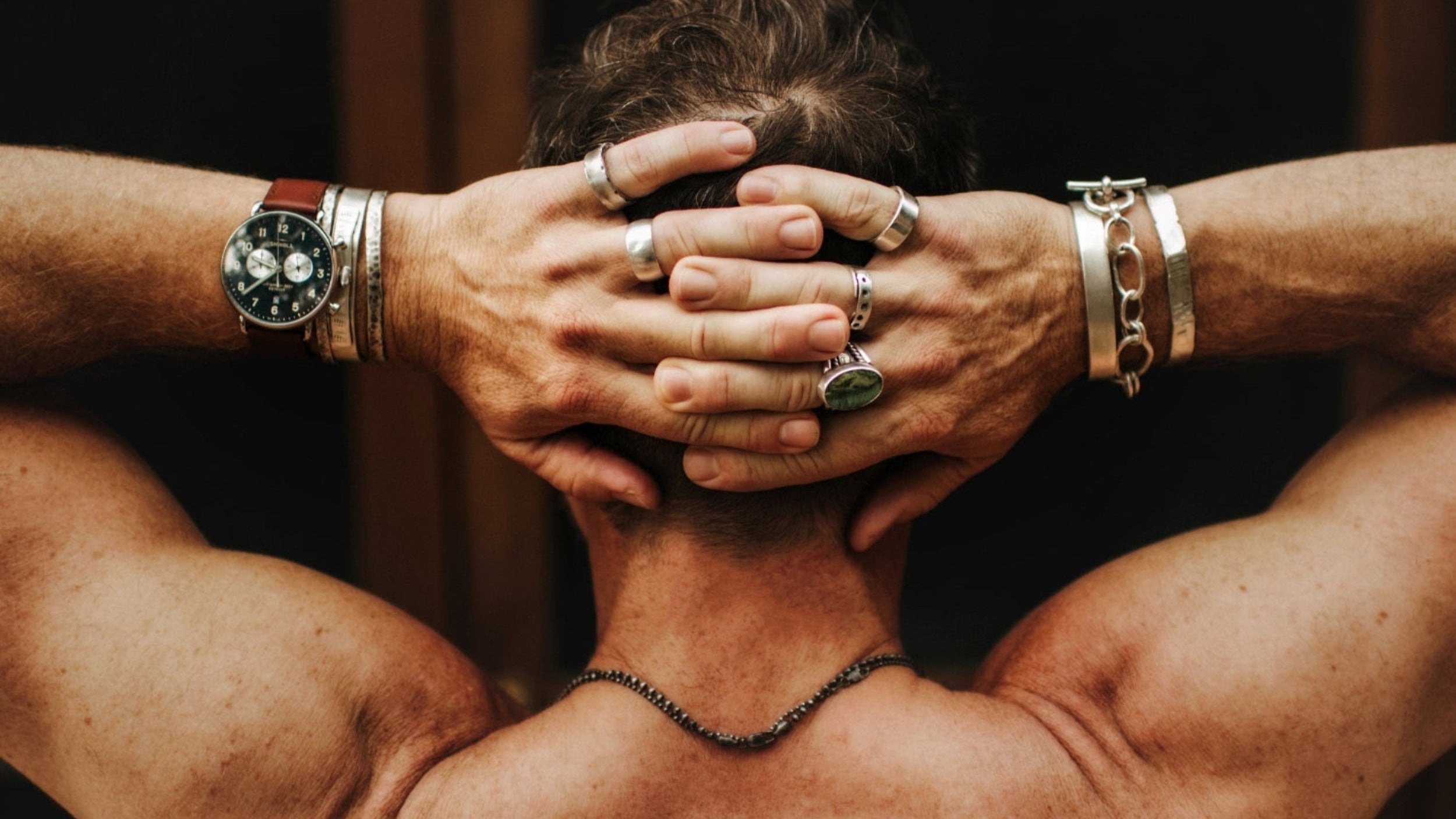 Muscular person with hands on head, wearing multiple bracelets and rings.